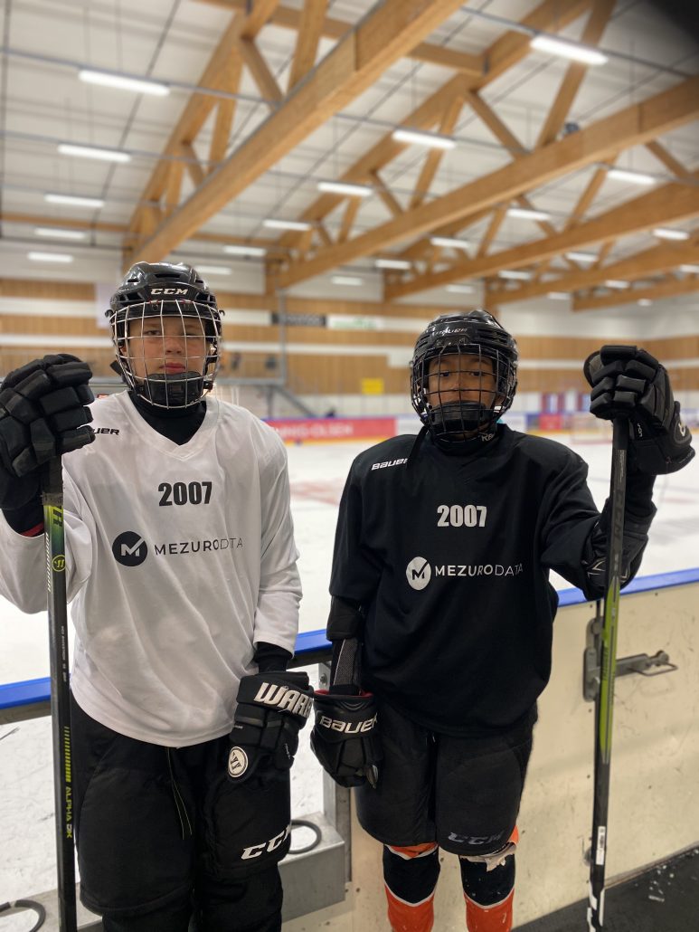 To gutter med ishockey utstyr står foran en isflate.