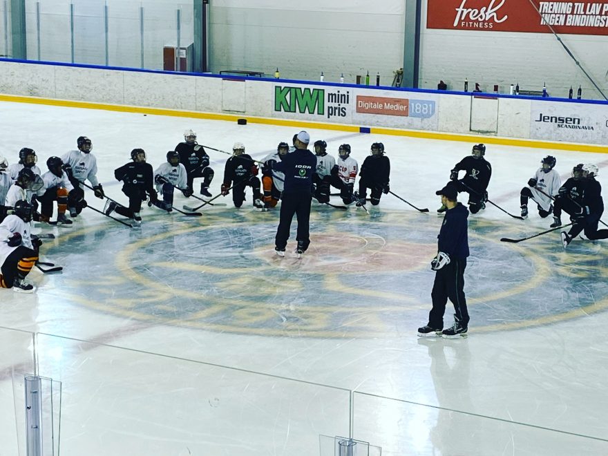 Barn som sitter på kne i ishockeyutstyr og lytter til trener