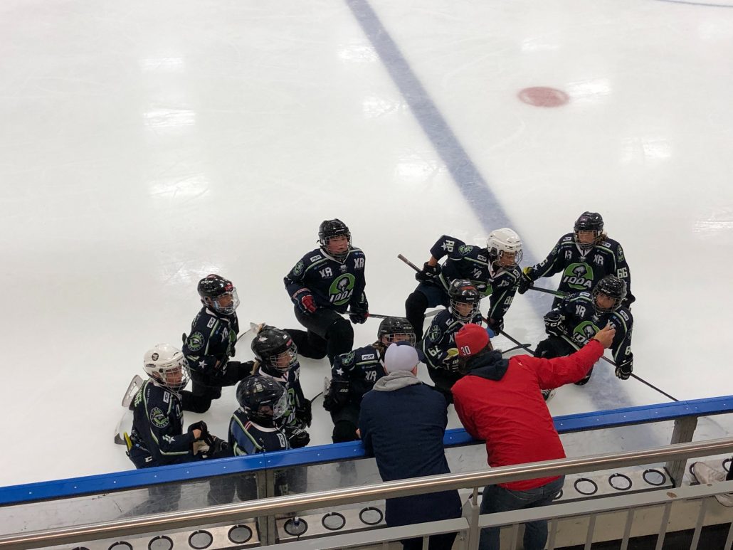 Ishockeyspillere sitter på isen og får peptalk fra to trenere.